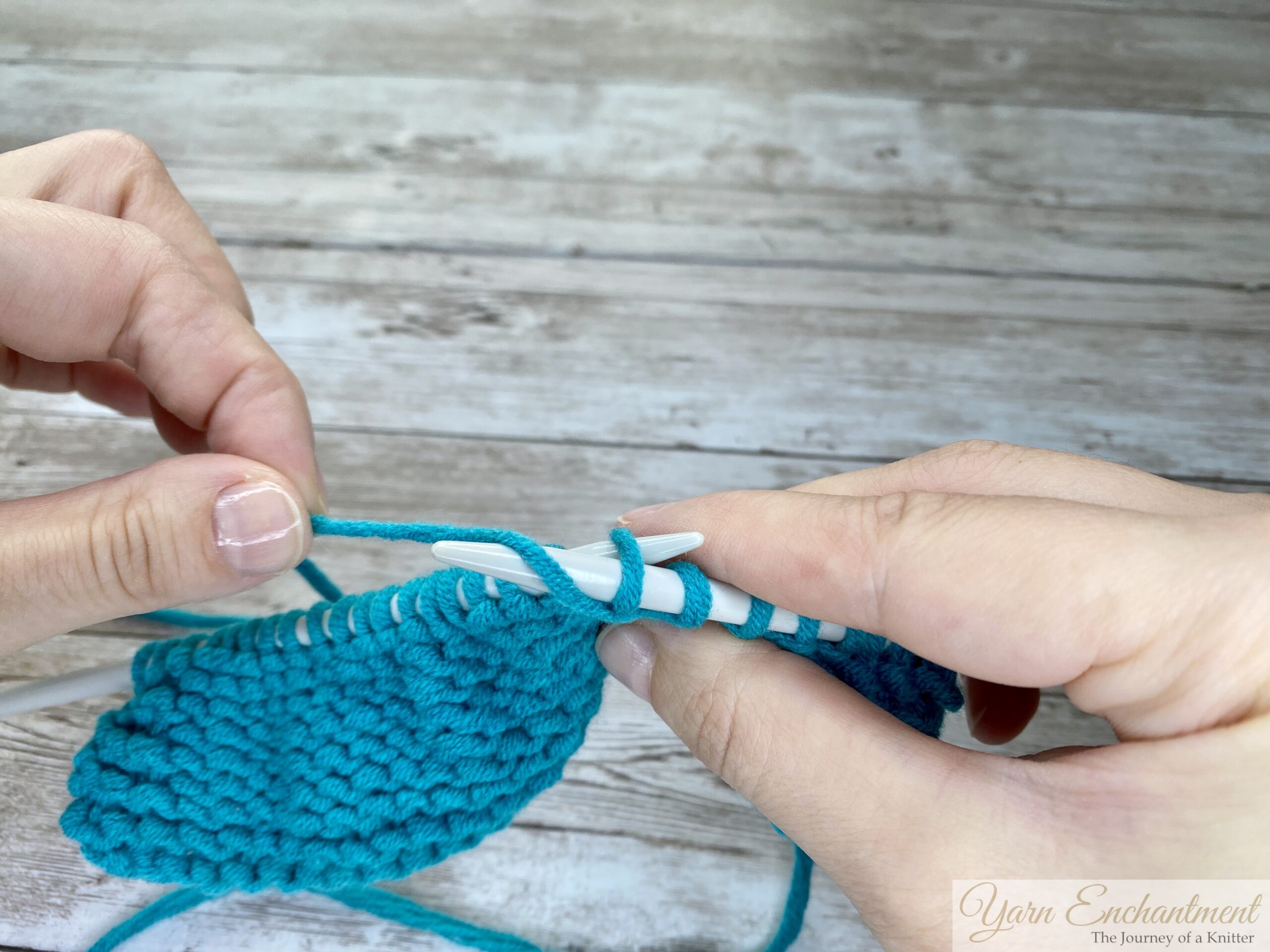 Close-up of hands pulling the right-hand knitting needle with turquoise yarn wrapped around it back through the stitch on the left-hand needle, creating a new loop to form the purl stitch.