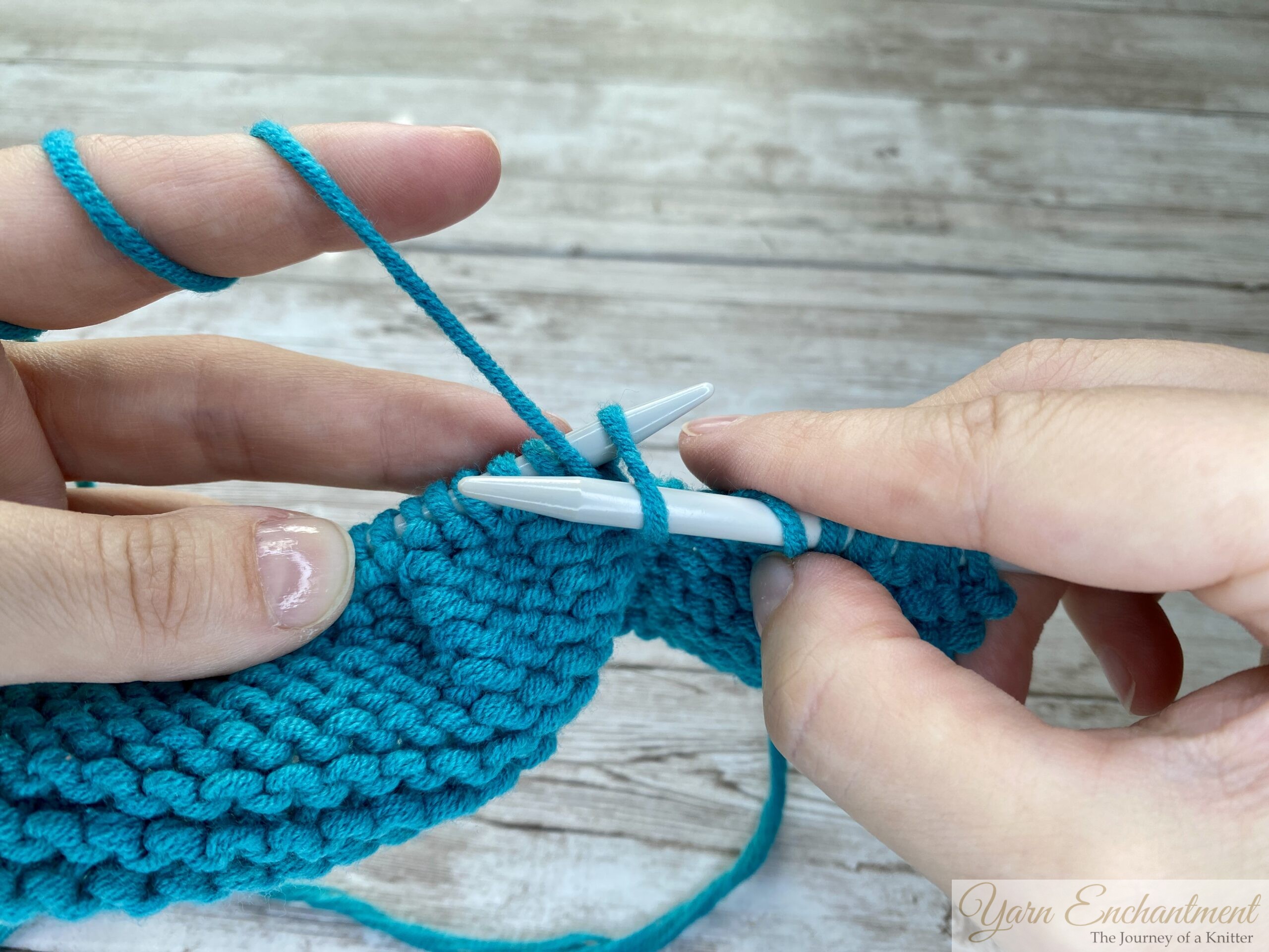 Close-up of hands showing the yarn wrapping around the needle in a clockwise direction.