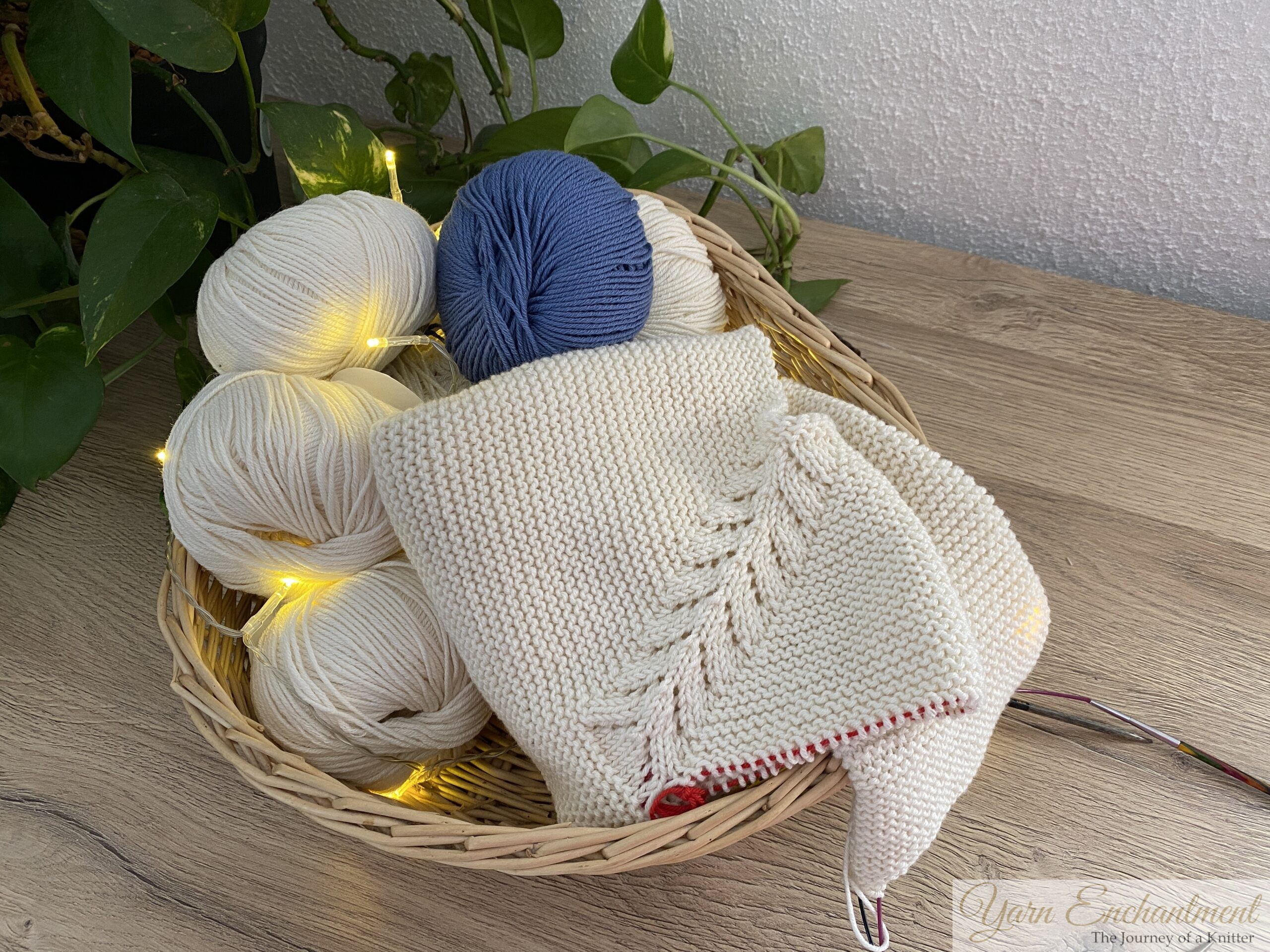 Personal knitting basket filled with cream and blue yarn balls, unfinished cardigan in progress, and circular needles—showing the real creative journey behind every project.