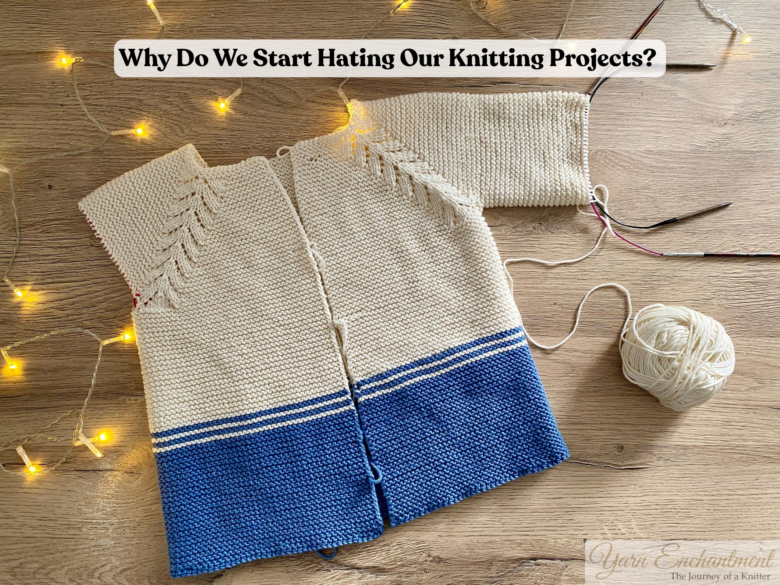 Unfinished hand-knitted cardigan in cream and blue yarn with circular needles, yarn ball, and fairy lights, illustrating knitting project frustration and the question ‘Why do we start hating our knitting projects?