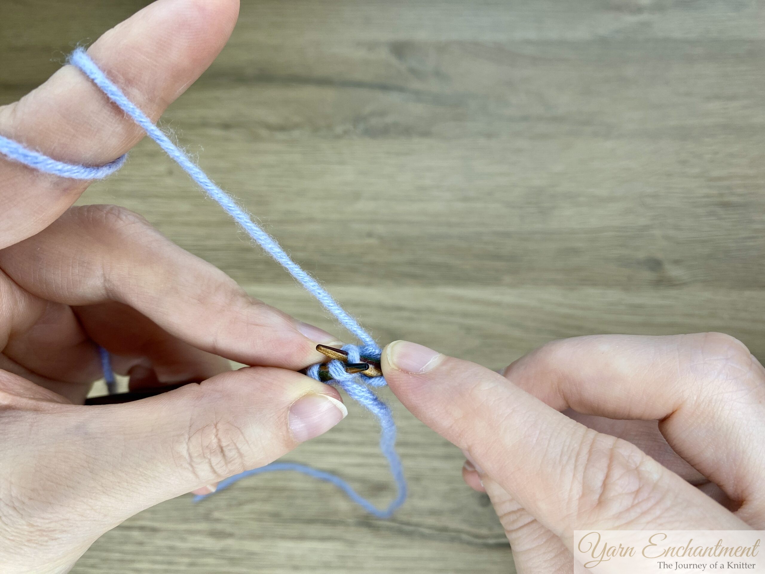 Close-up of hands knitting an i-cord; the working yarn is wrapped around the index finger, and the needle is inserted into the first stitch, ready to knit.