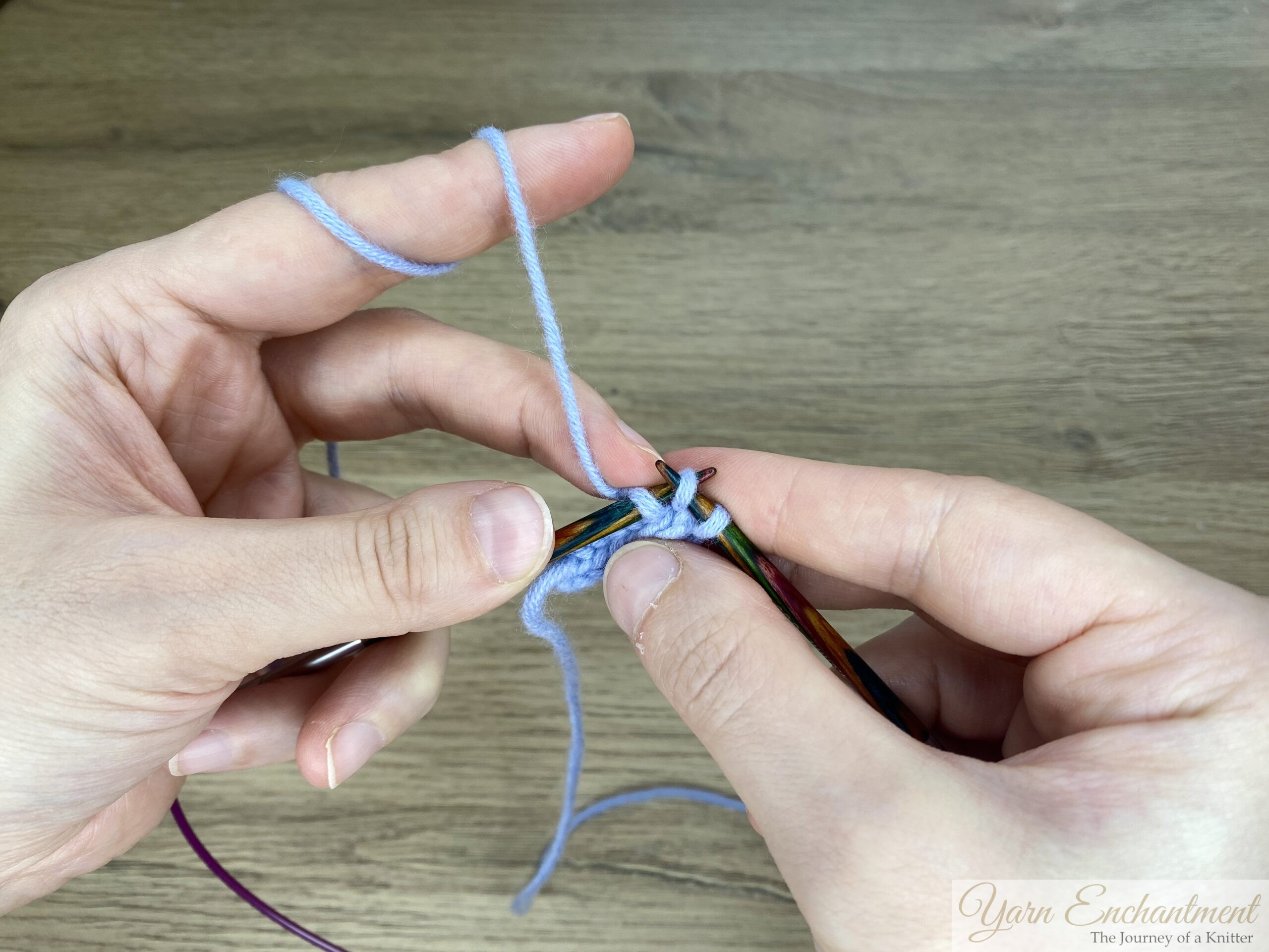 Close-up of hands knitting an I-cord using circular knitting needles with blue yarn, showing stitches on the needle.