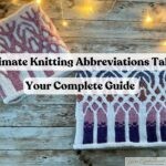two hand-knitted cowl scarves with intricate colorwork patterns in pink, purple, and white, displayed on a rustic wooden surface with warm string lights, illustrating the Ultimate Knitting Abbreviations Table guide.