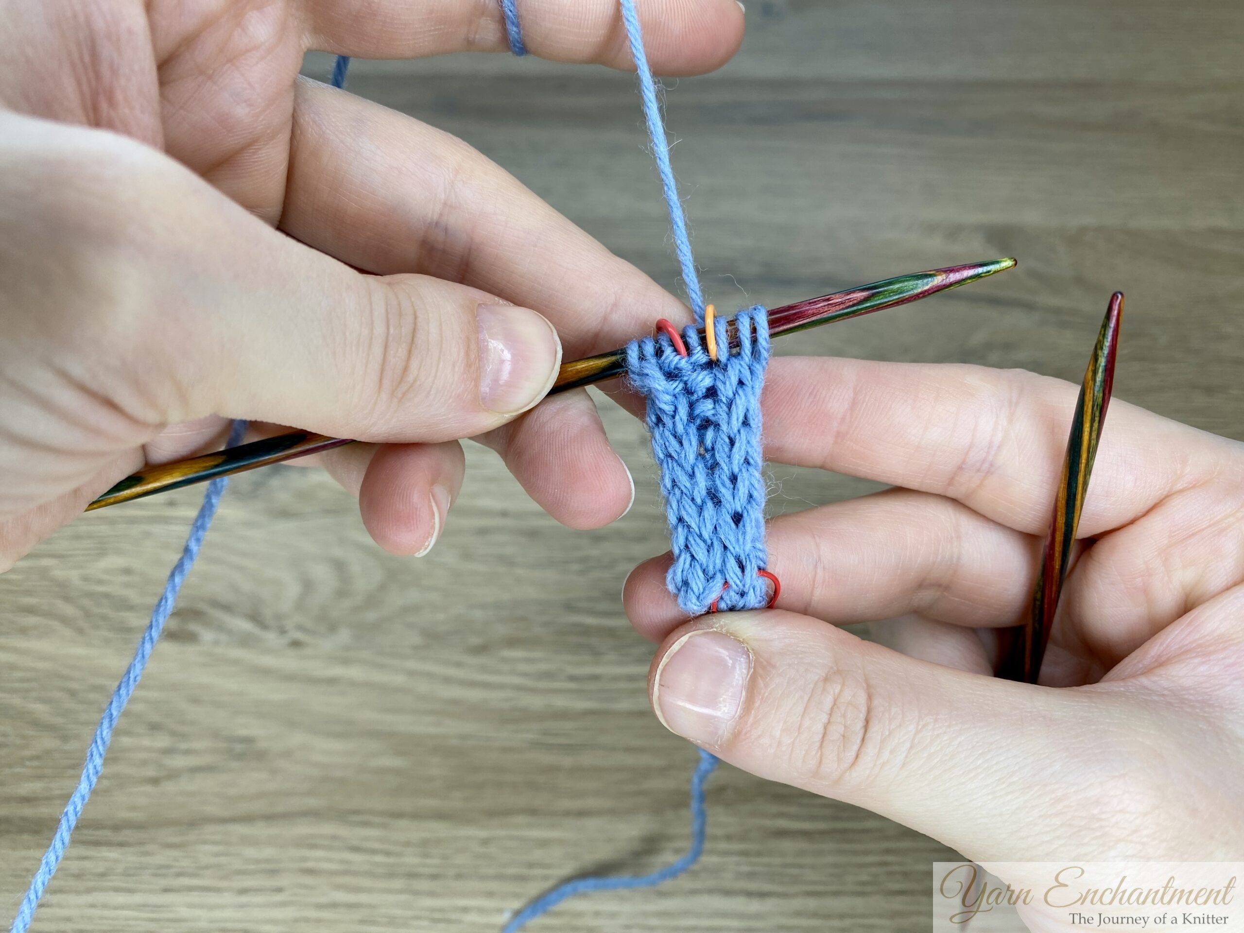 Blue garter-stitch Sophie-style swatch with neat I-cord edges and stitch markers on a wooden needle, showing the result of the alternative increase method.