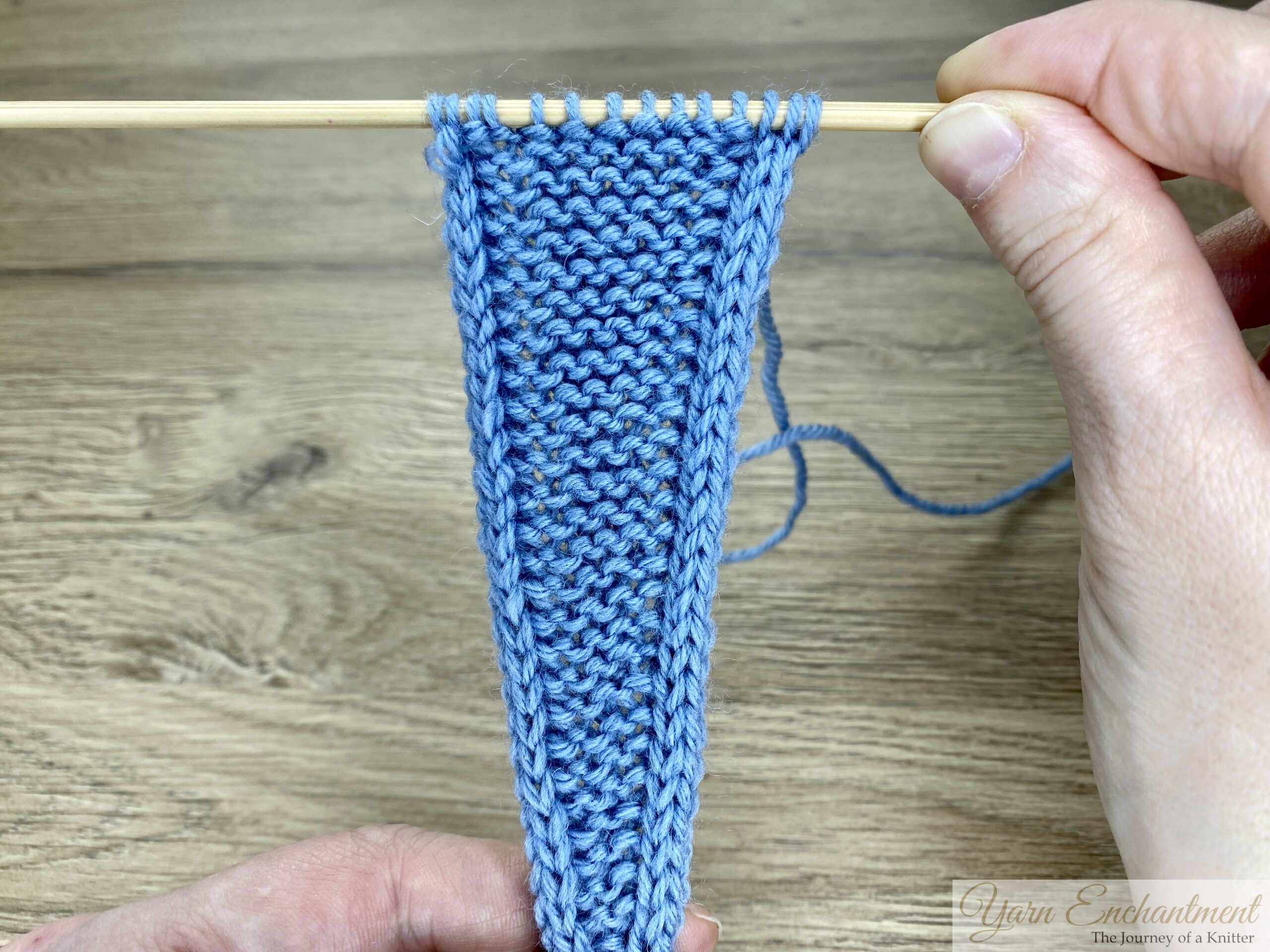 Blue garter-stitch Sophie-style swatch with neat I-cord edges and stitch markers on a wooden needle, showing the result of the alternative increase method.