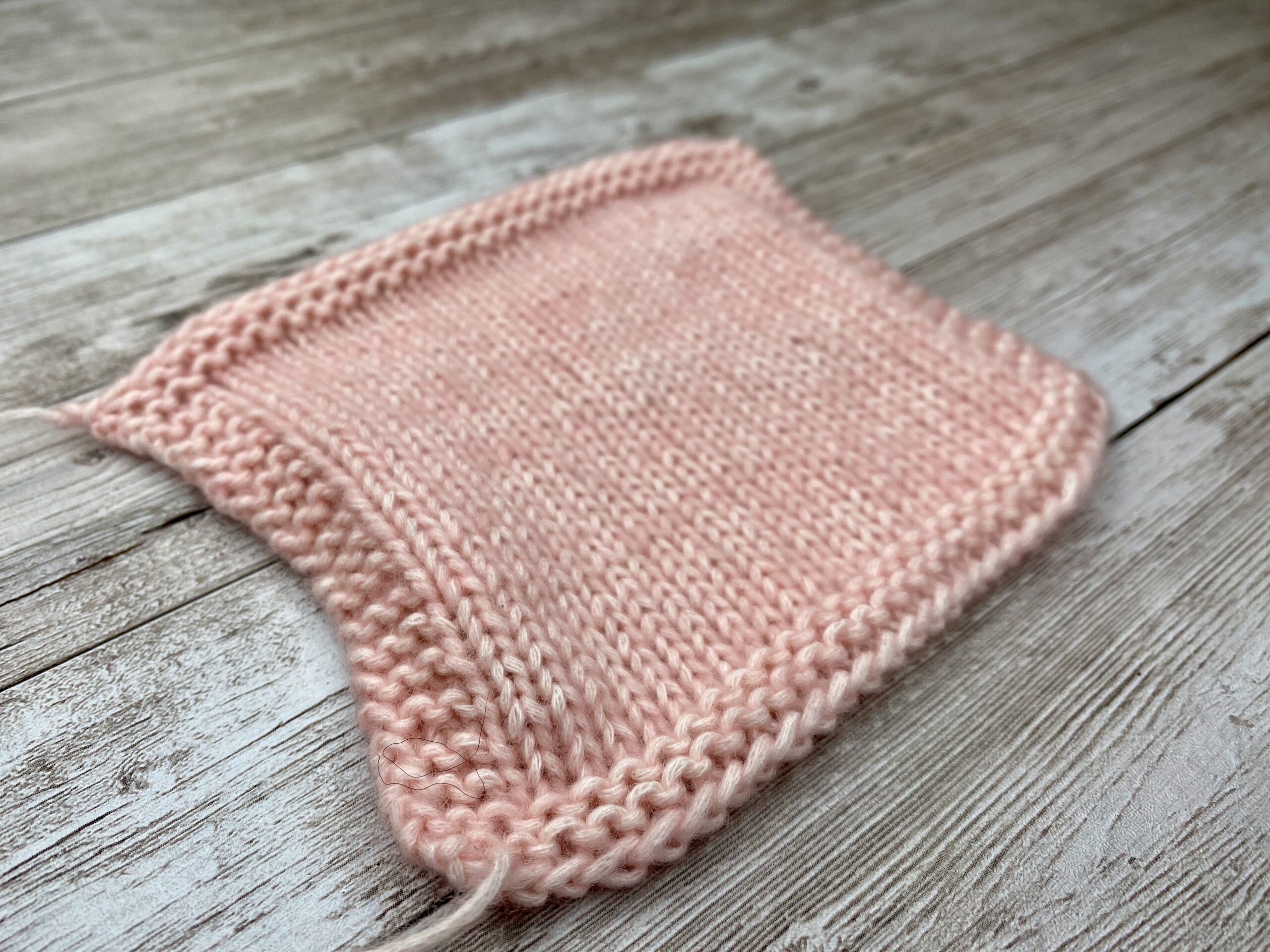 Angled close‑up of pink stockinette gauge swatch with garter stitch frame around the edges.