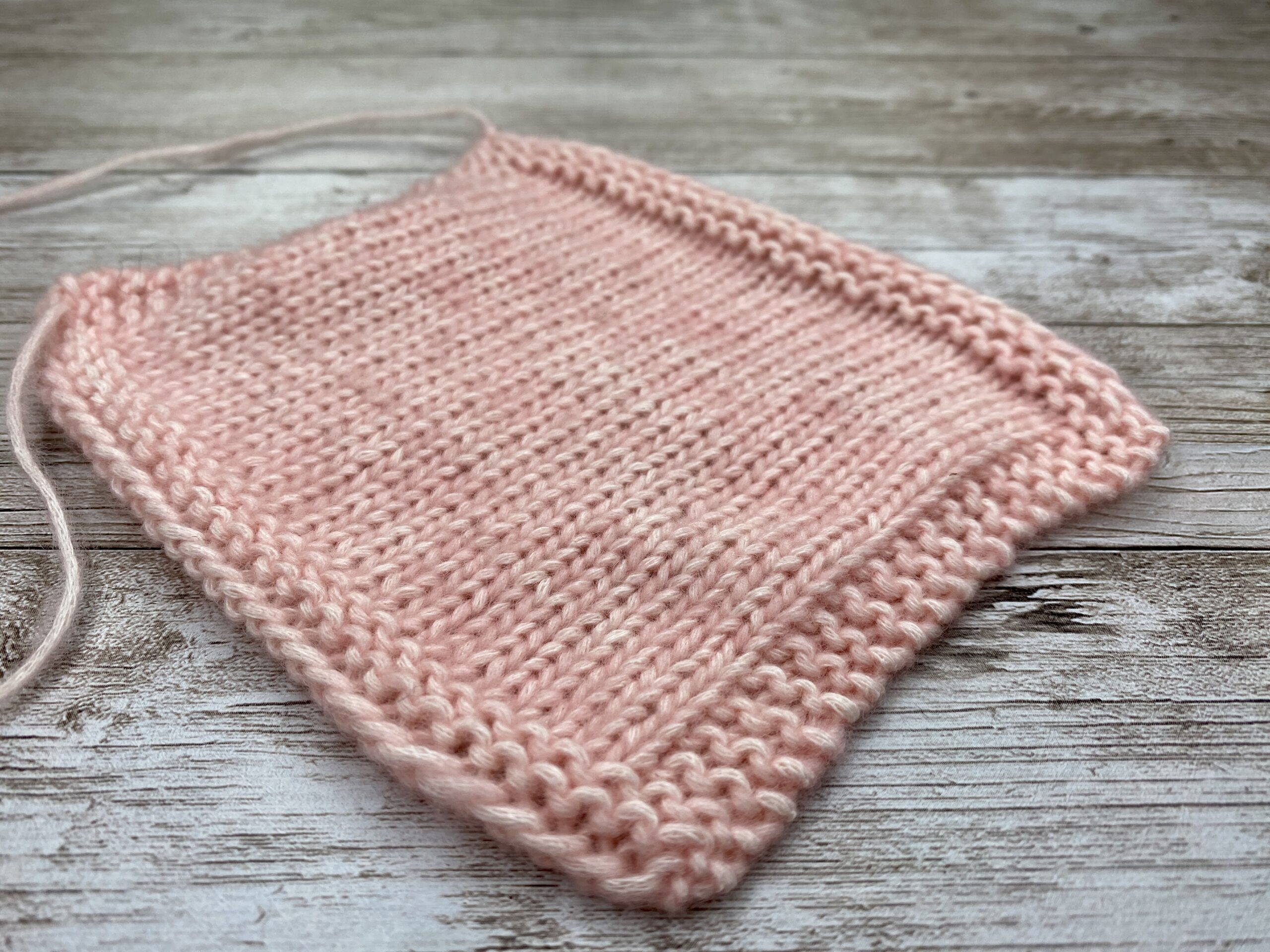 Angled close‑up of pink stockinette gauge swatch with garter stitch frame around the edges.