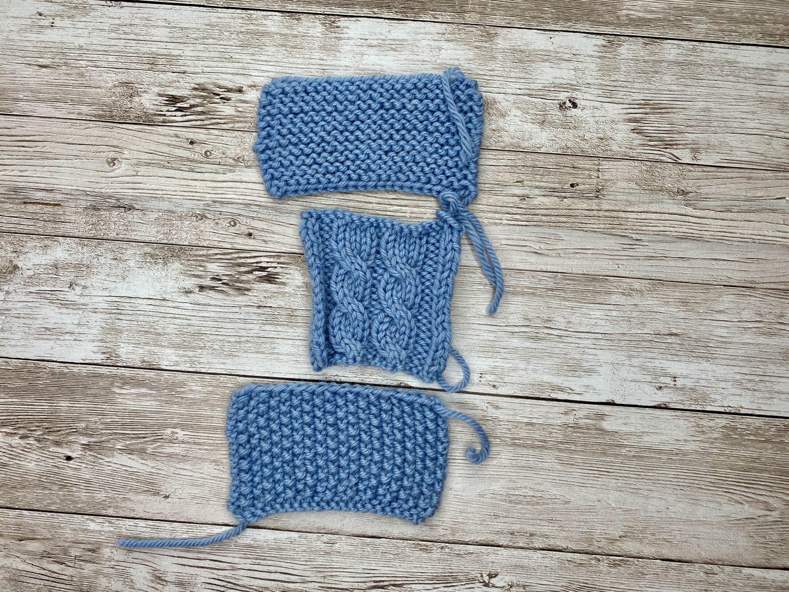 Three blue gauge swatches stacked vertically: garter border, cabled centre, and garter border sections.