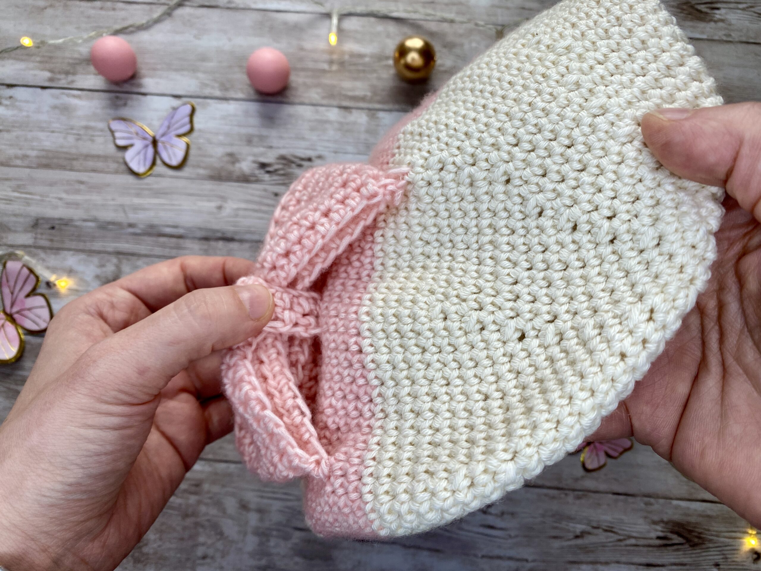 Side view of a cream and blush crochet beanie with a big pink bow, showing the textured stitches and soft yarn.