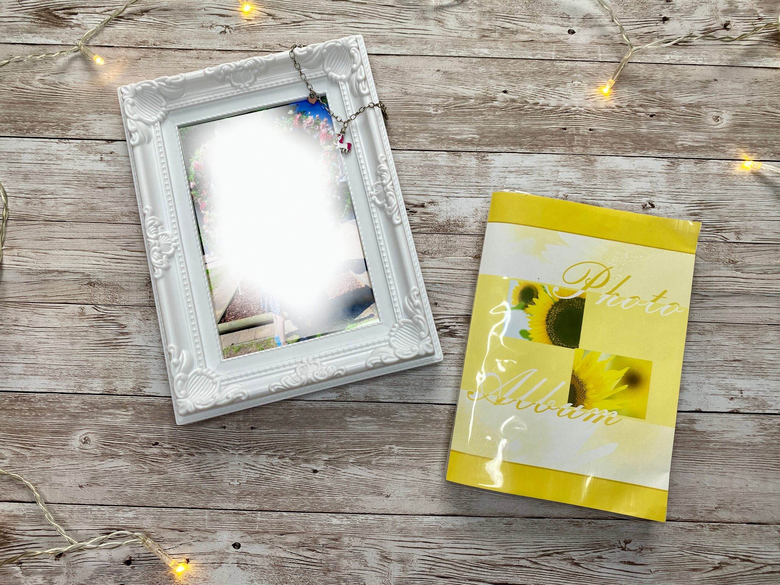 White photo frame with a blurred family picture next to a yellow photo album on a wooden background, representing a sentimental handmade photo gift.