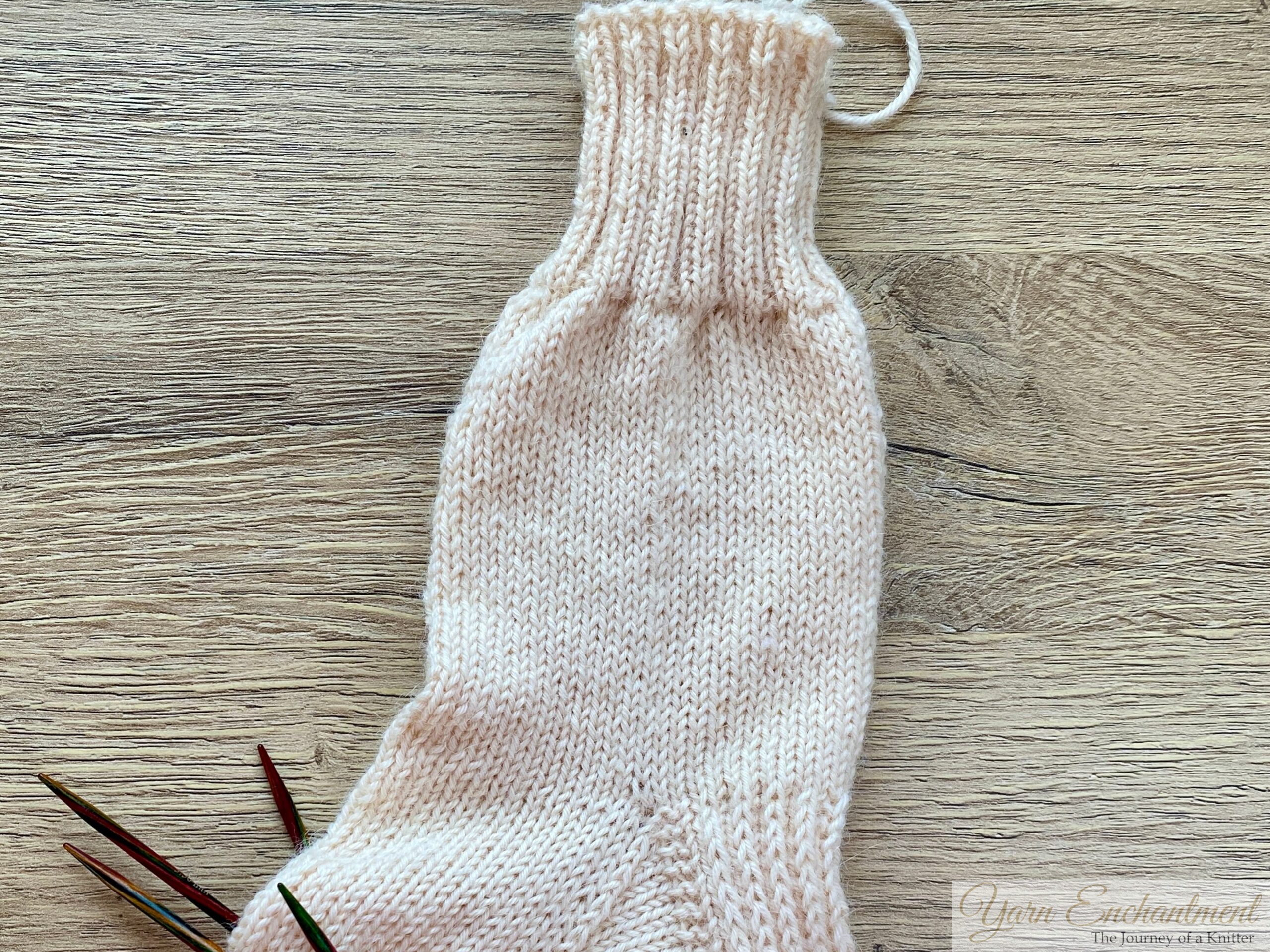 Knitted alpaca sock showing uneven stitch tension, with needles nearby on a wooden surface