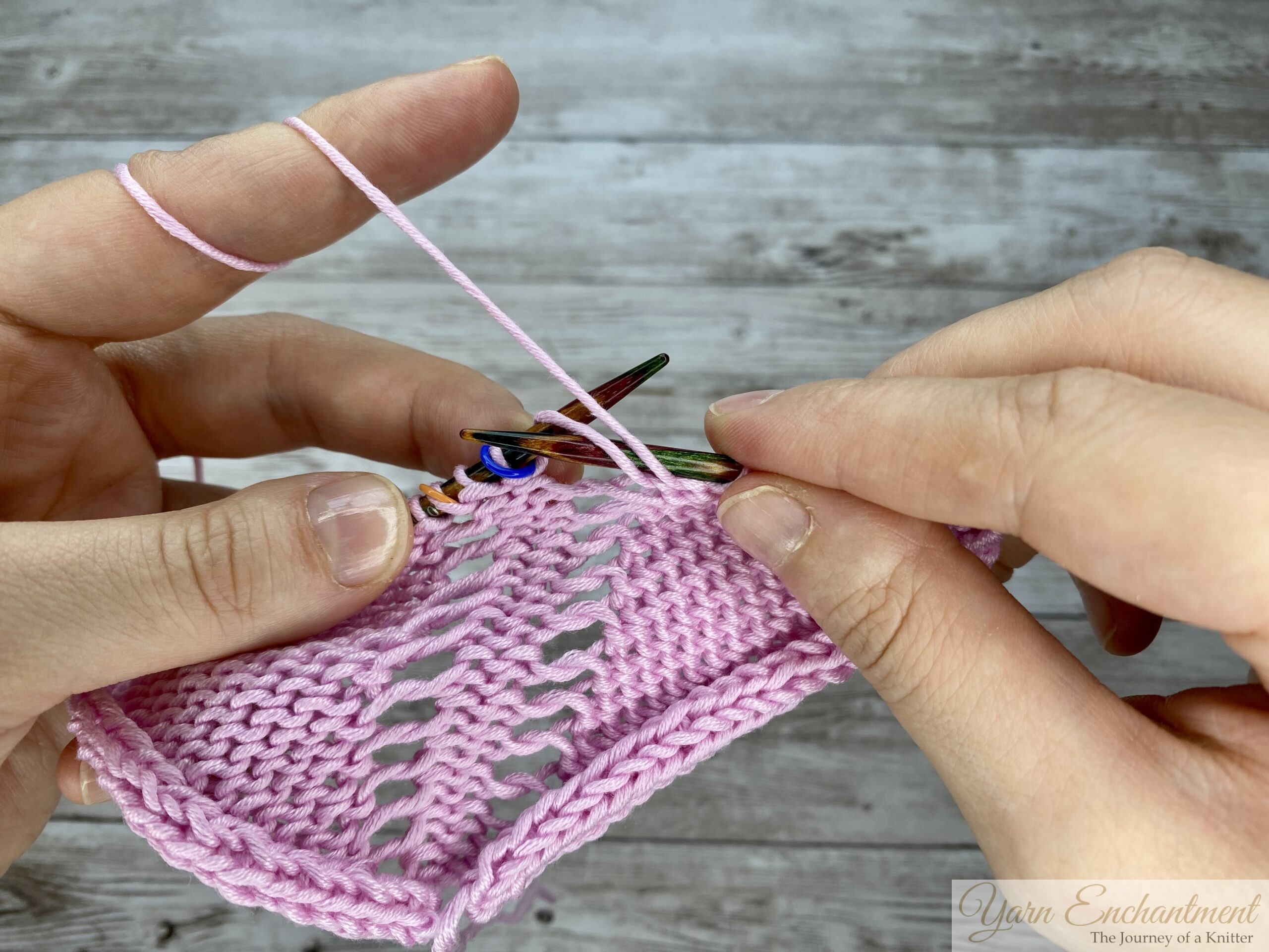 Wrapping the pink working yarn around the right needle to perform a purl through the front loop on the wrong side of the knitting project.
