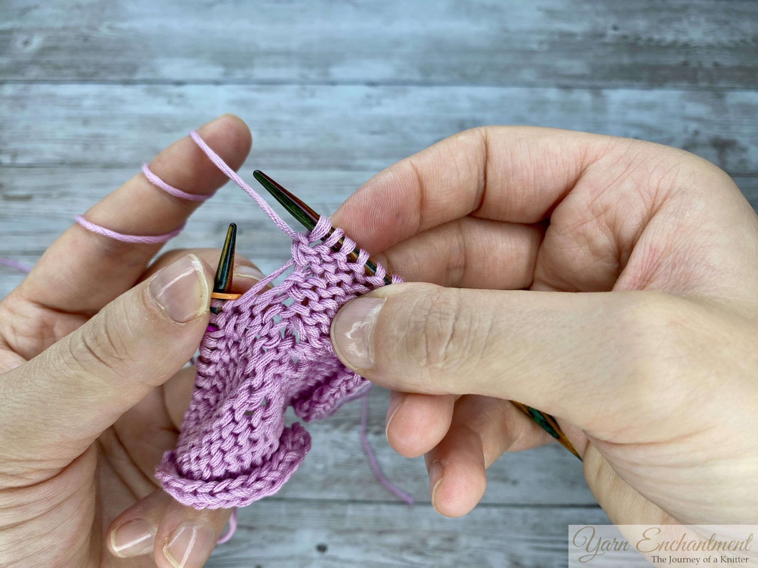 Finished purl-through-back-loop stitch showing a neat, hole-free increase on the pink knitted garter stitch fabric.