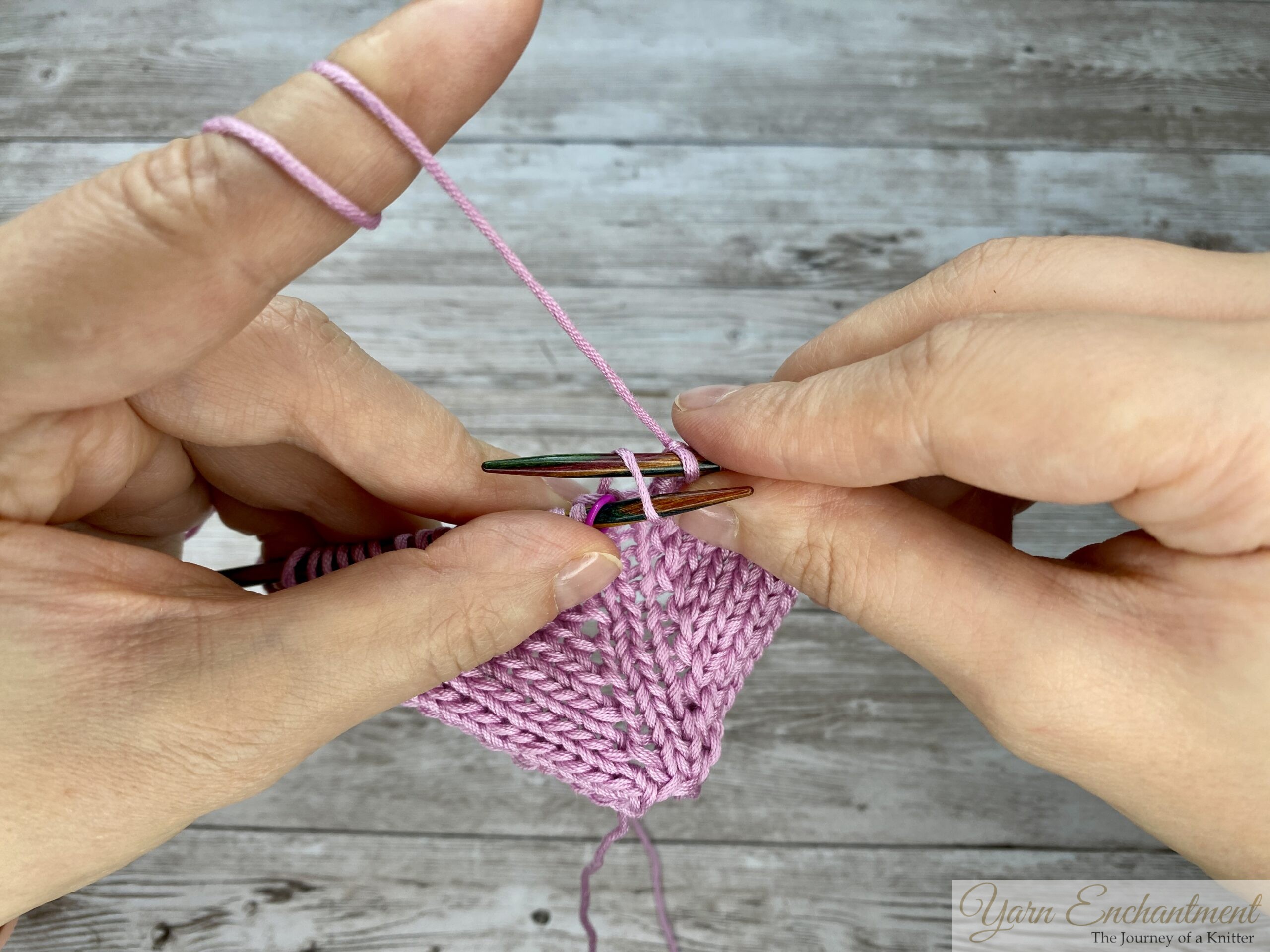 The right needle wraps the working pink yarn over the top to create the yarn-over loop, a key step for making open increases in circular lace knitting.
