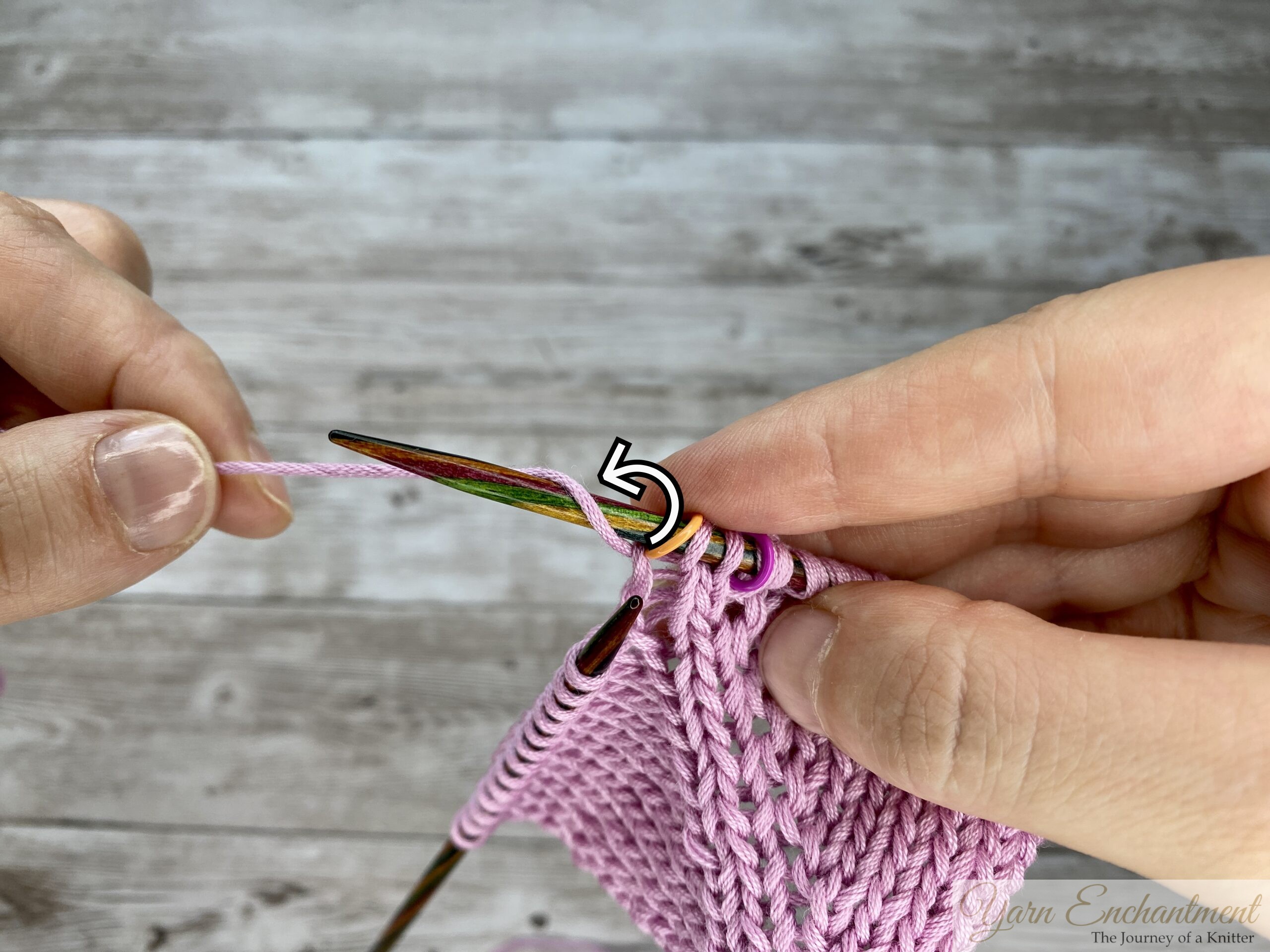 Close-up of a directional M1L left-leaning yarn-over increase on pink knitted fabric, showing a hand wrapping the yarn forward over the needle with a graphic arrow indicating the correct direction.