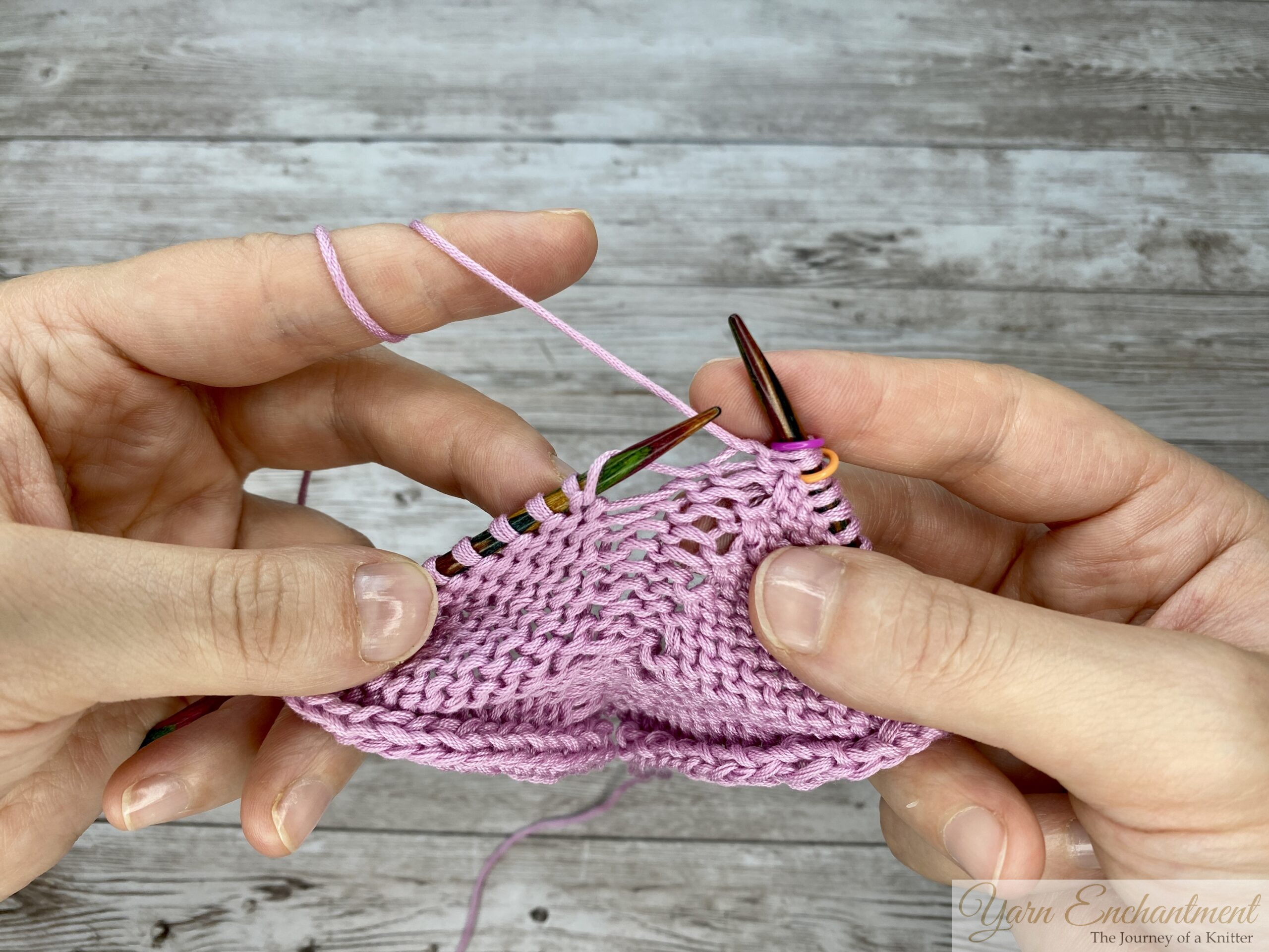Completing the directional yarn wrap for a Make 1 Right (M1R) increase while knitting with pink cotton yarn on circular needles in the round.