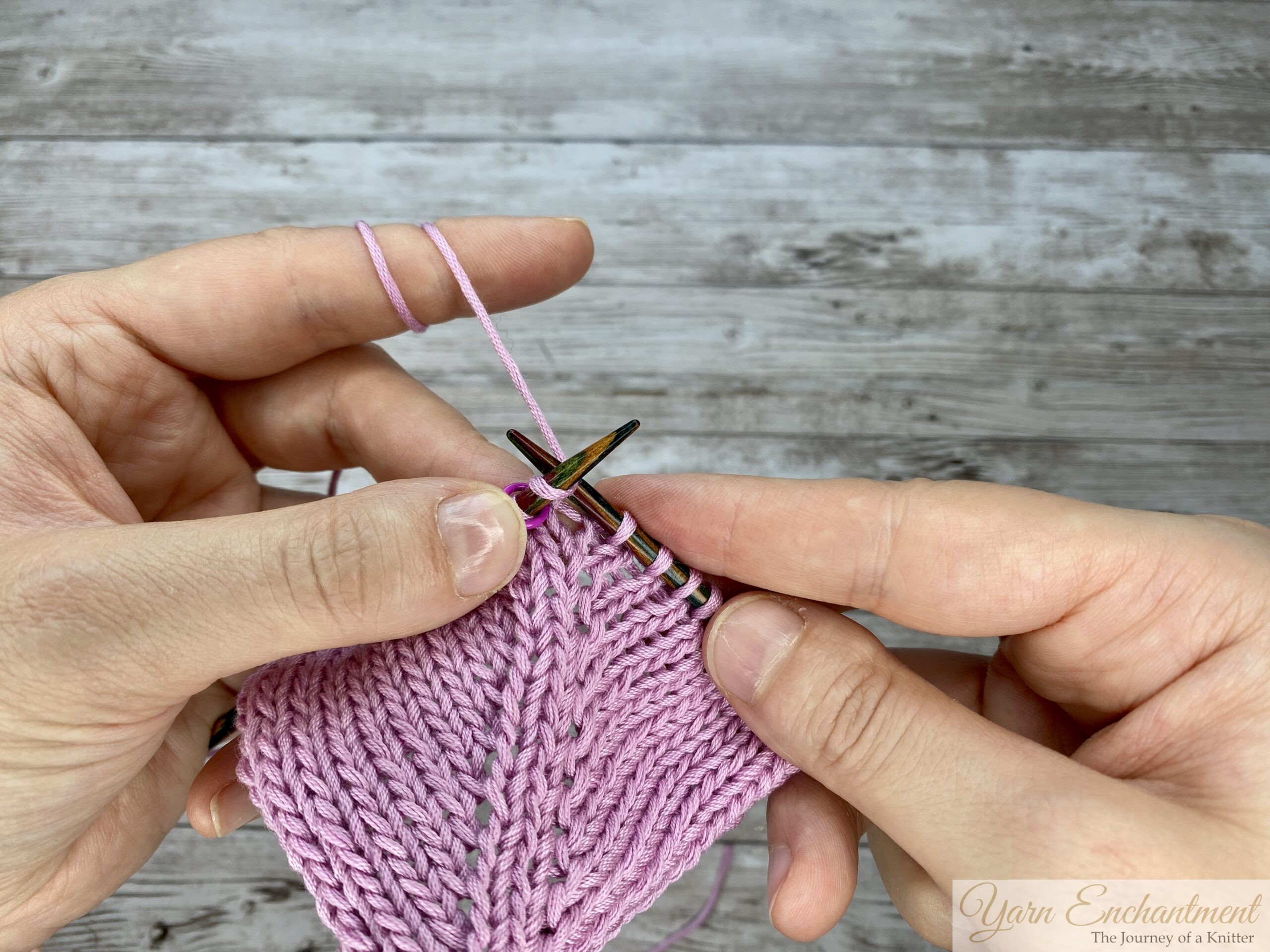 Wrapping the working pink yarn around the right needle to complete the knit stitch located right after the M1R directional loop, while knitting in the round.