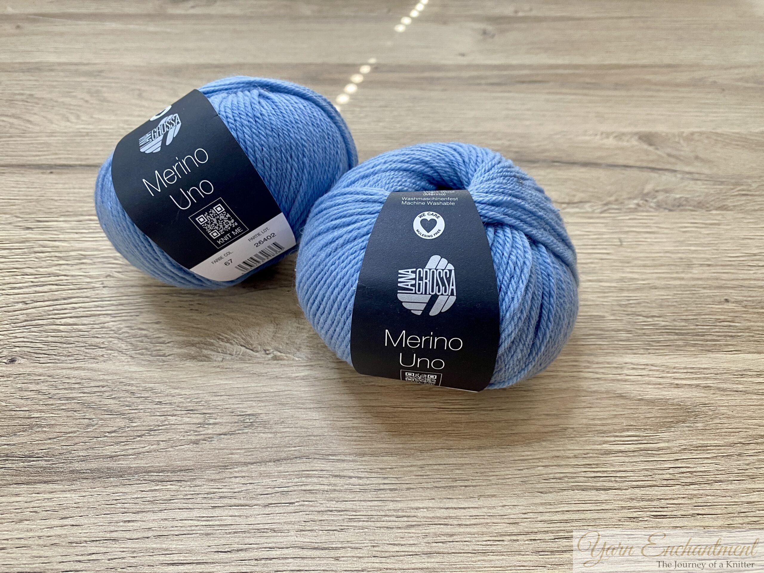 Two skeins of light blue Lana Grossa Merino Uno yarn with black and white labels, placed next to each other on a rustic wooden table.
