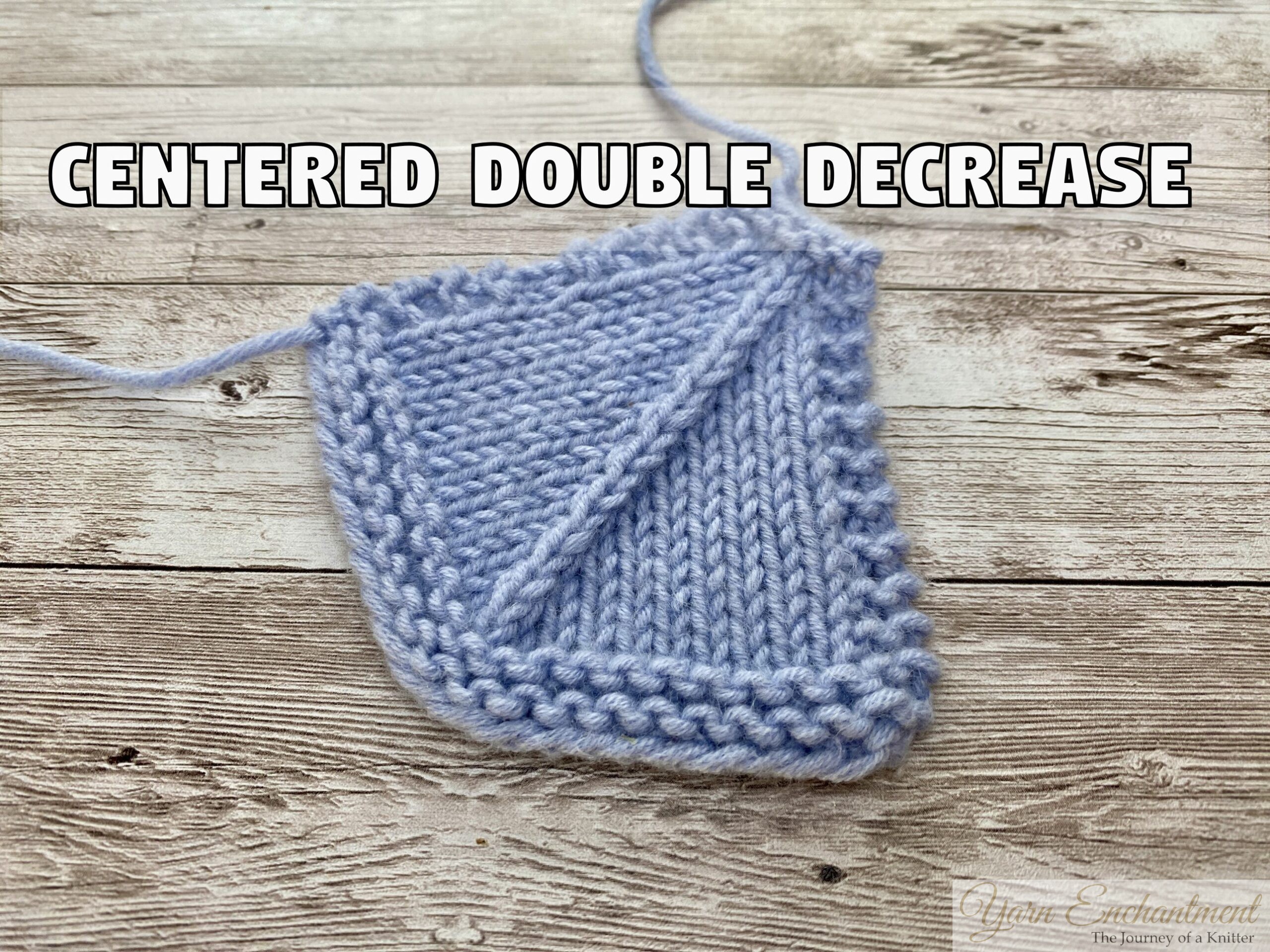 A light blue knitted swatch resting on a wooden surface, demonstrating a 'Centered Double Decrease' in knitting. The stitch pattern shows a distinct, straight diagonal line moving upwards from left to right through the center of the stockinette fabric, bordered by garter stitch edges. Bold white text with a black outline reading 'CENTERED DOUBLE DECREASE' is overlaid at the top of the image.
