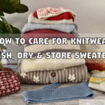 A cozy stack of folded knitted sweaters in various colors (red, pink, blue, cream) sits on a wooden floor next to a green potted plant. Scattered around the stack are knitted accessories, including a red and white patterned hat, a blue scarf, and small mittens. Large text overlays the image reading: 'HOW TO CARE FOR KNITWEAR' and 'WASH, DRY & STORE SWEATERS'.