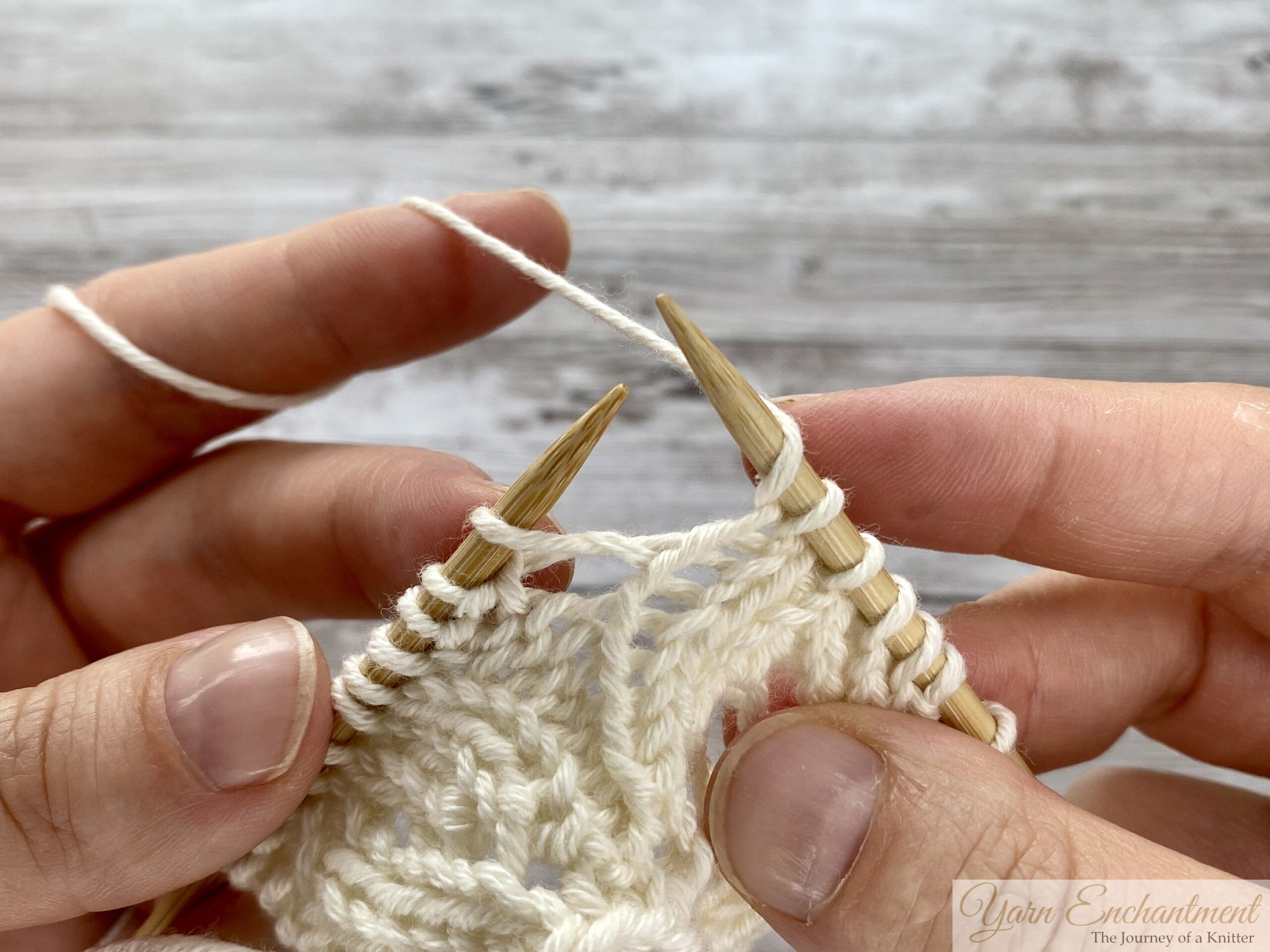 Close-up of hands knitting. The yarn has been wrapped over the right needle to create the yarn over loop. The right needle tip is now positioned to enter the next knit stitch.