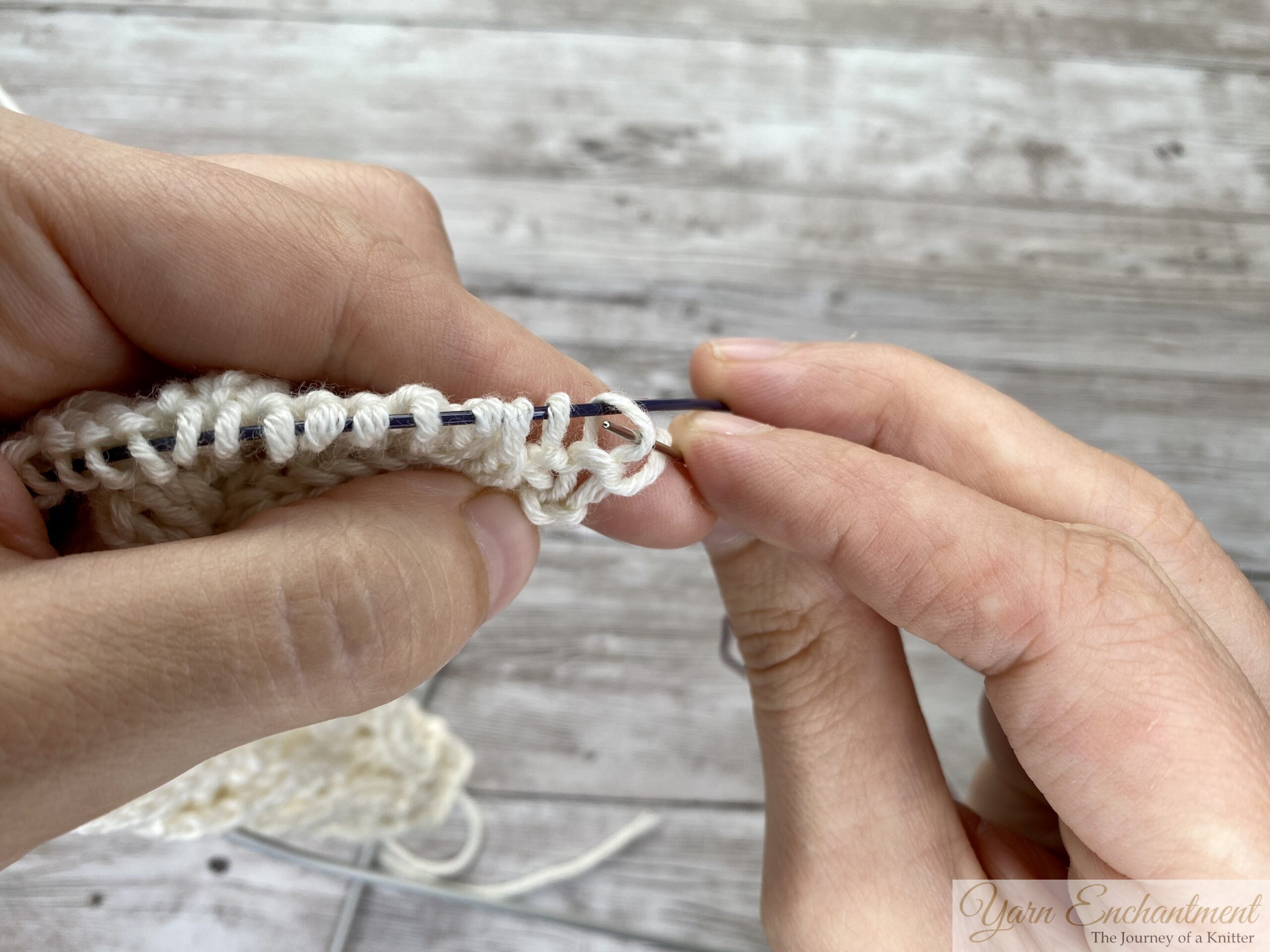 Tapestry needle through the first stitch loop on a circular needle cable, starting a lifeline in cream lace knitting.