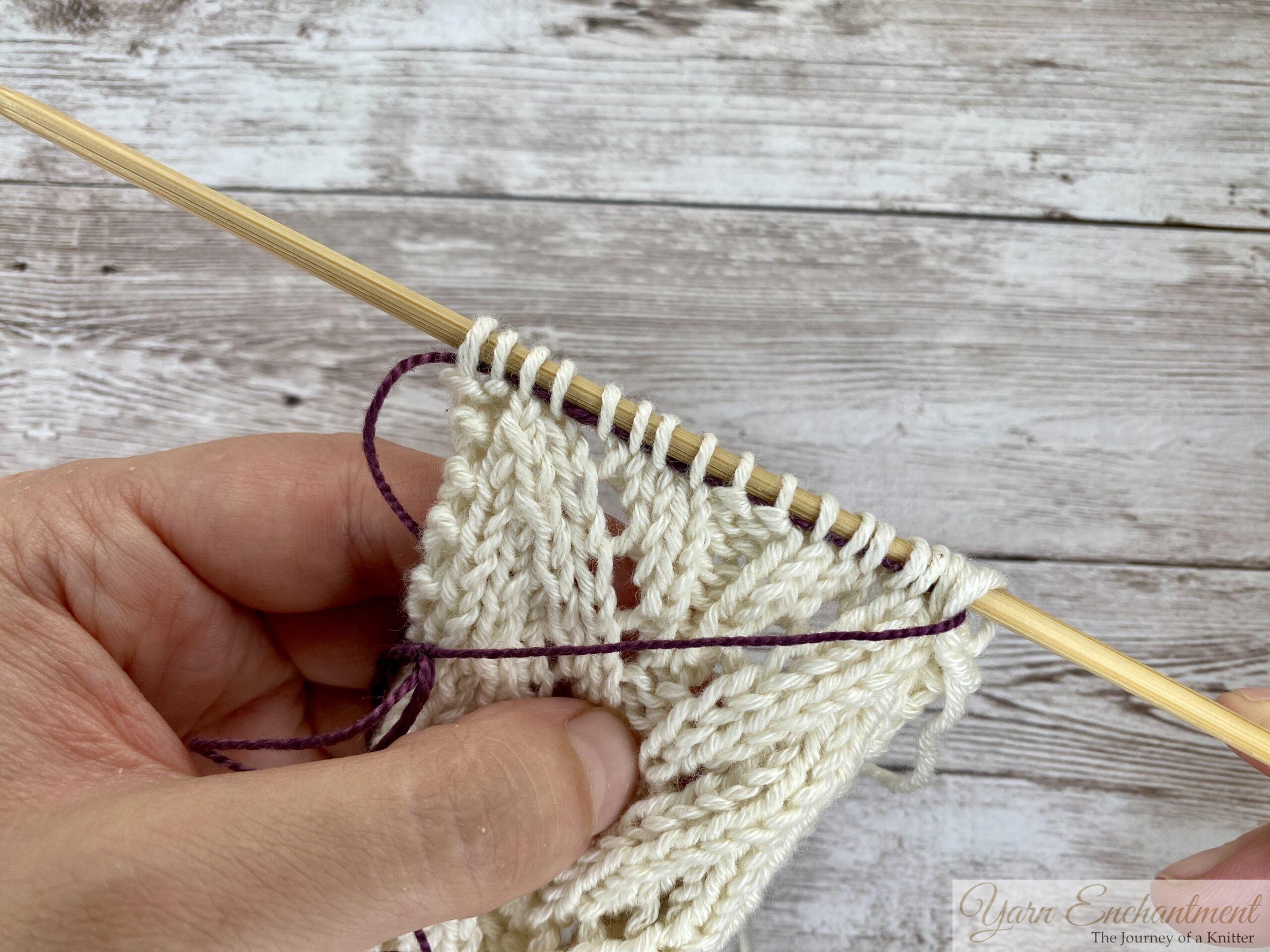 Stitches slipped back onto a wooden needle above the purple lifeline, ready to keep knitting.