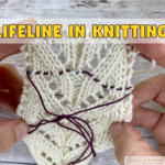 Hands stretch an ivory lace swatch to show a plum contrast lifeline threaded through one row of stitches, knotted below