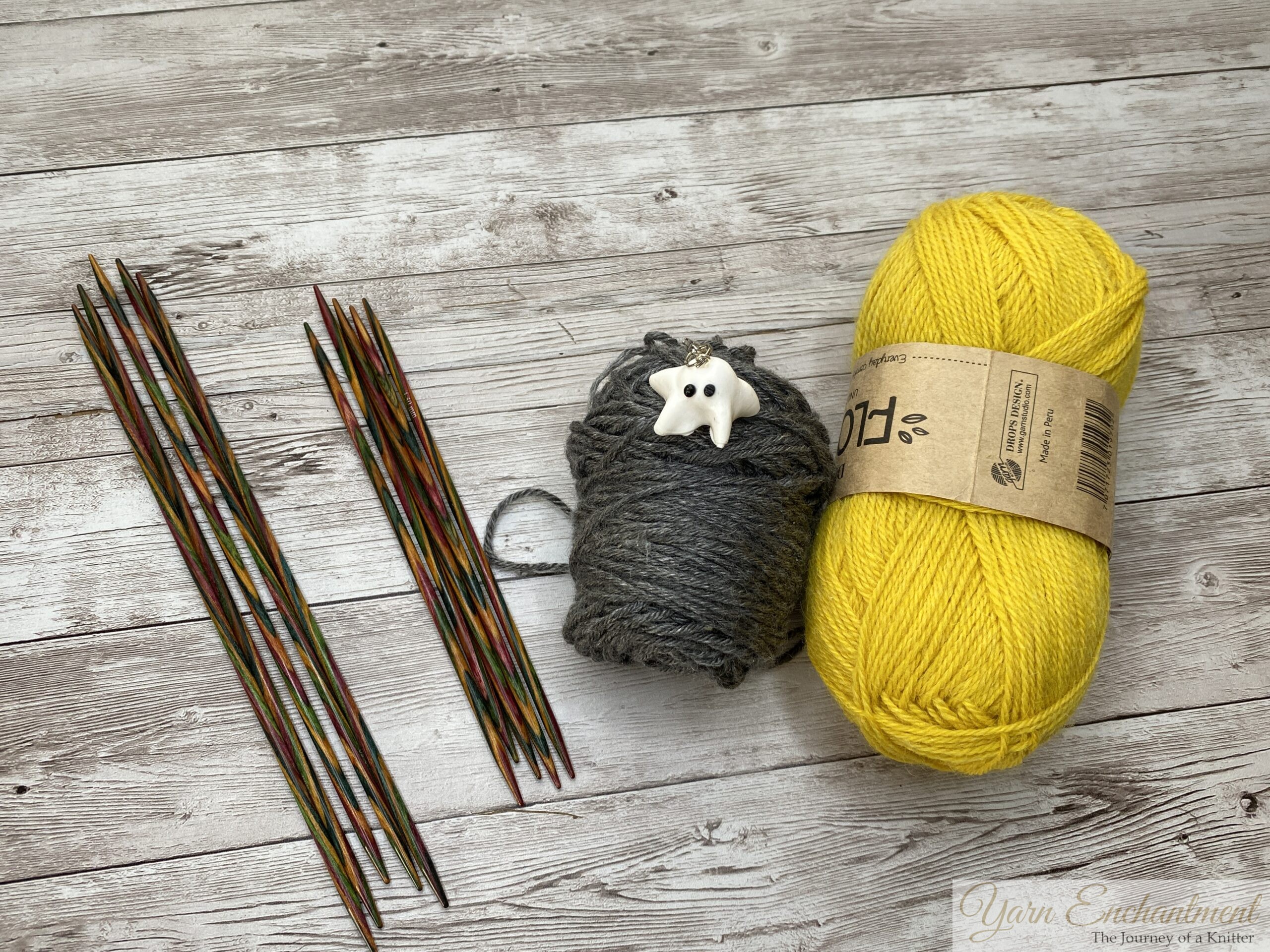Ruffle cuff edge project materials: yellow Drops yarn, gray mini skein with ghost stitch marker, and colorful wooden double-pointed needles