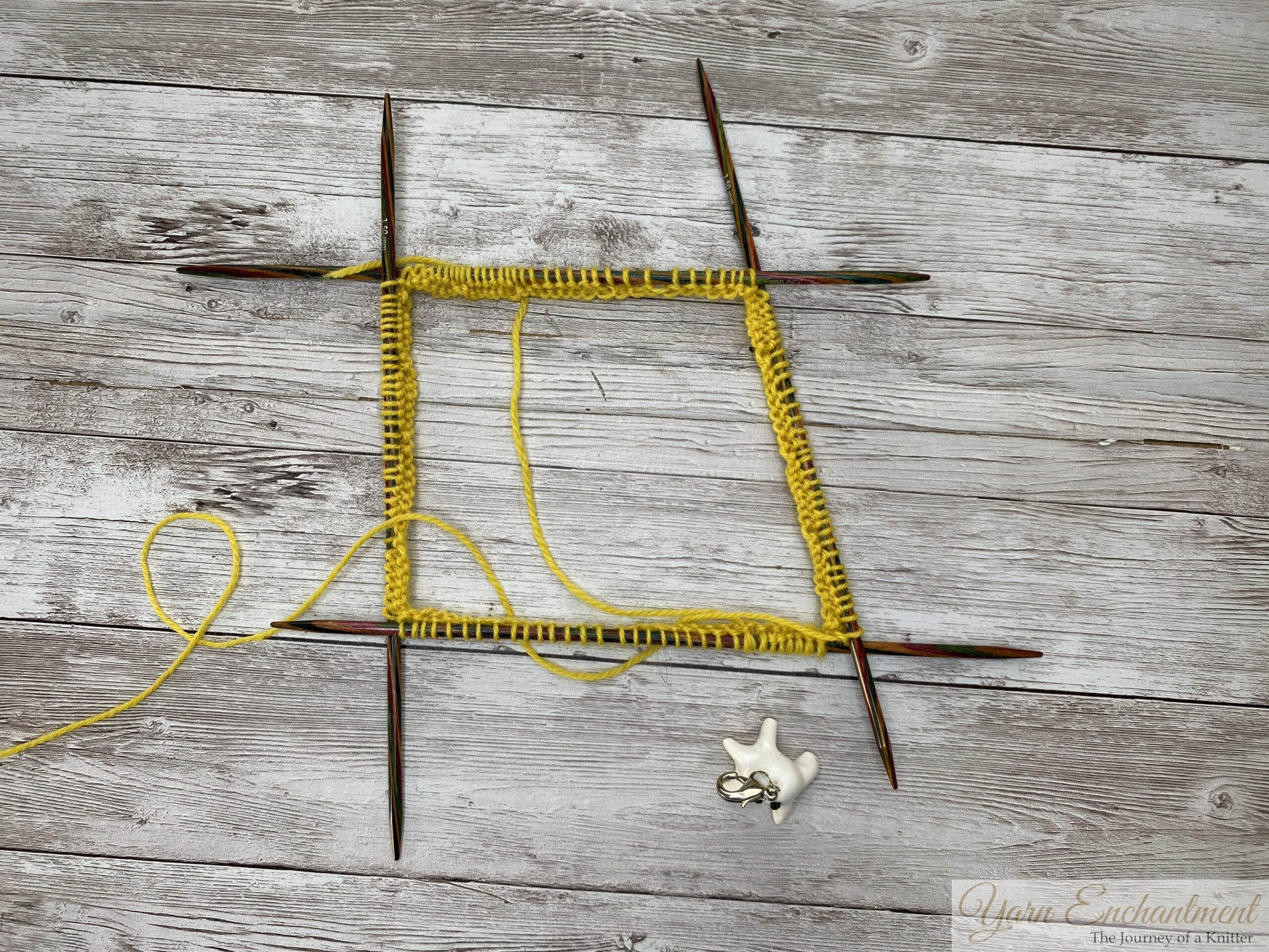 Yellow ruffle sock cuff cast-on stitches divided evenly across four wooden double-pointed needles, joined in the round