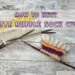 Two sock cuffs with ruffled edges in yellow and cream yarn resting on wooden knitting needles